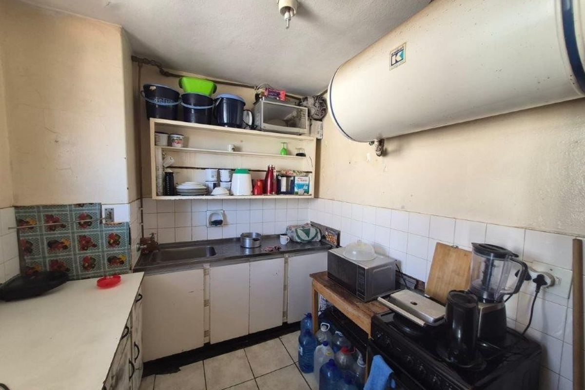 A dated kitchen featuring basic cabinetry, tiled splashbacks, and an exposed electric water heater, offering significant potential for modernization and renovation.