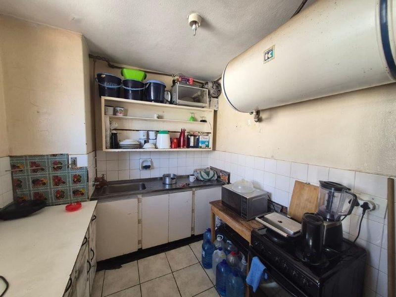 A dated kitchen featuring basic cabinetry, tiled splashbacks, and an exposed electric water heater, offering significant potential for modernization and renovation.