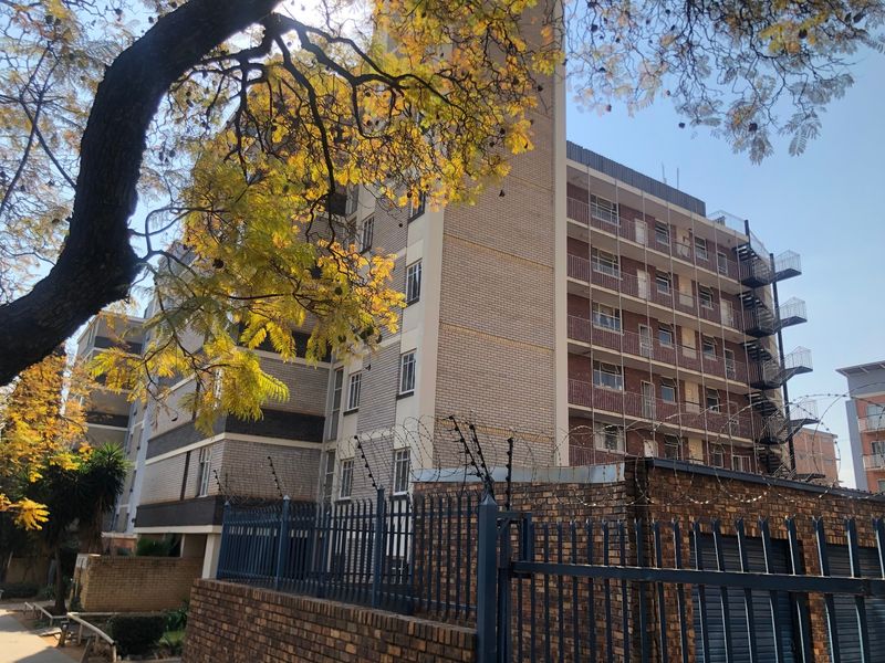 Exterior view of a multi-story apartment building featuring brick facade, private balconies, and secure perimeter fencing with electric security wires.