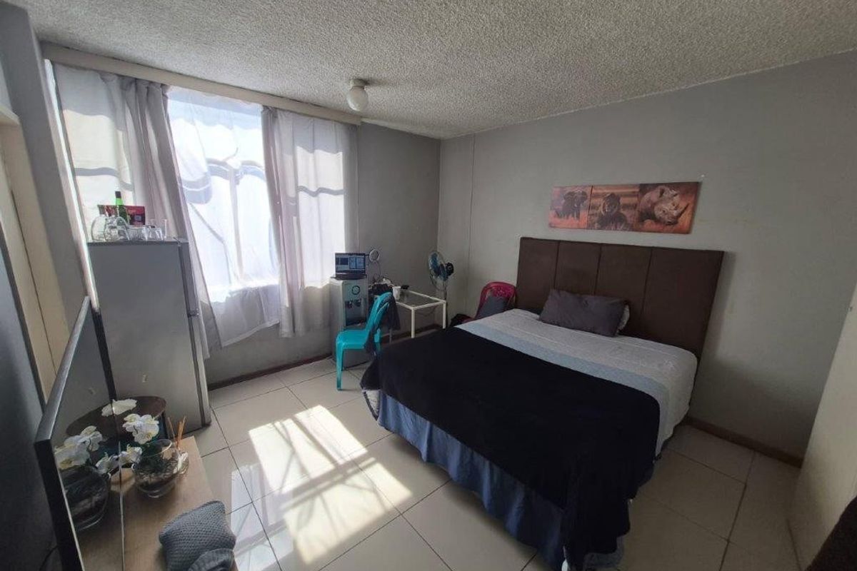 A functional bedroom featuring tiled flooring and a textured ceiling, providing a neutral base for potential interior updates.