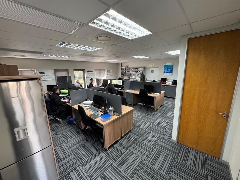 A functional open-plan office space featuring modular workstations, carpeted flooring, and recessed ceiling lighting, suitable for a professional work environment.