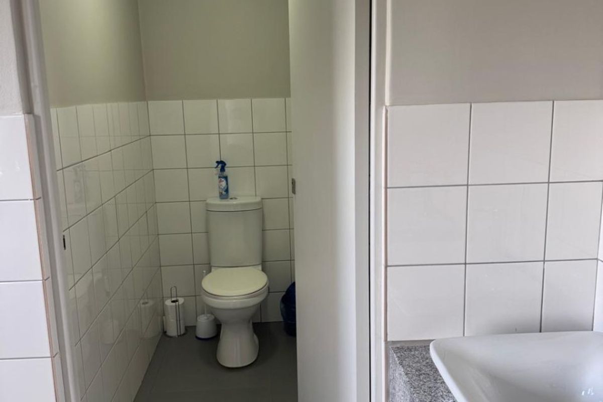 A clean, functional office restroom featuring a white toilet, a modern washbasin with a granite countertop, and neutral tiled wall finishes.