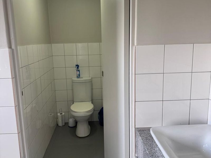 A clean, functional office restroom featuring a white toilet, a modern washbasin with a granite countertop, and neutral tiled wall finishes.
