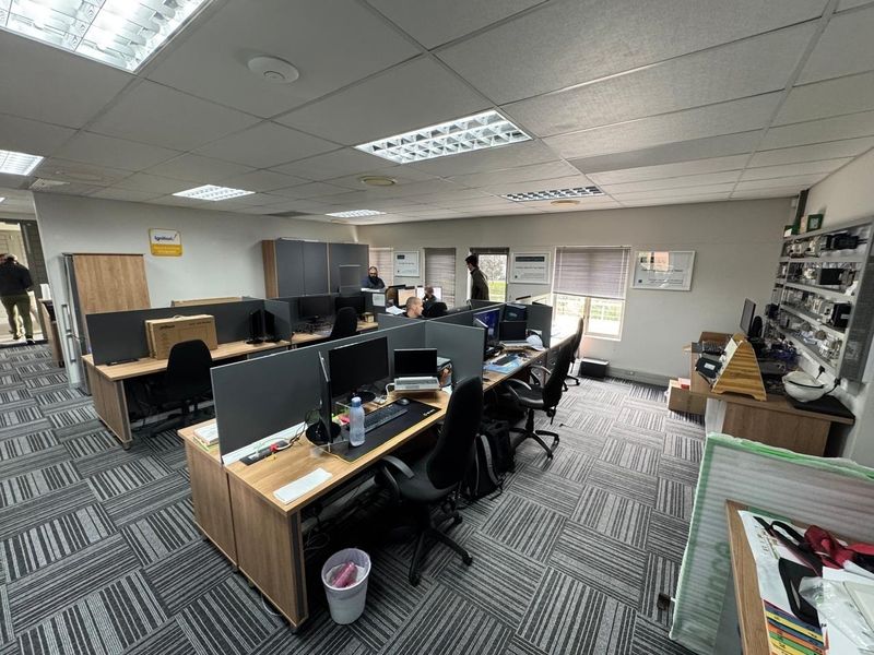 Open-plan office space featuring carpet tiles, suspended ceilings with recessed lighting, and built-in workstation partitions.