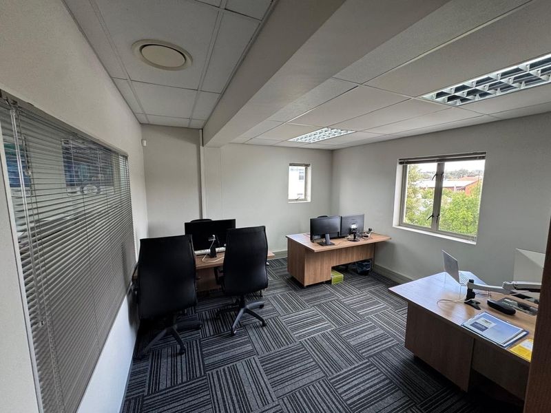 A functional office space featuring carpet tiles, suspended ceilings with recessed lighting, and large windows with venetian blinds, providing a professional work environment.
