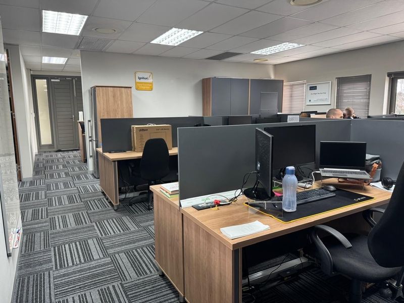 A functional open-plan office space featuring modular workstations with privacy partitions, carpet tile flooring, and integrated storage cabinetry under a suspended ceiling.