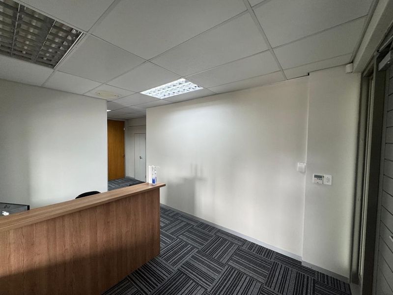 A professional office reception area featuring a built-in wooden desk, modern carpet tiles, and a suspended ceiling with integrated lighting.