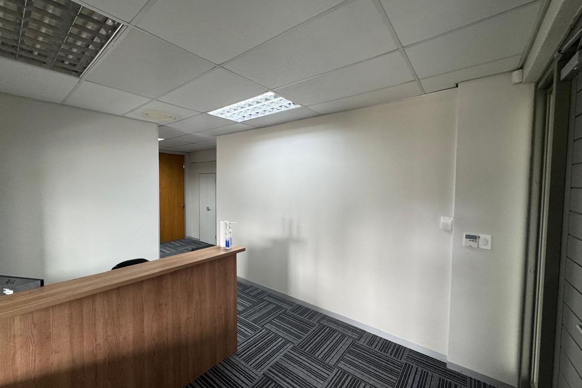 A professional office reception area featuring a built-in wooden desk, modern carpet tiles, and a suspended ceiling with integrated lighting.
