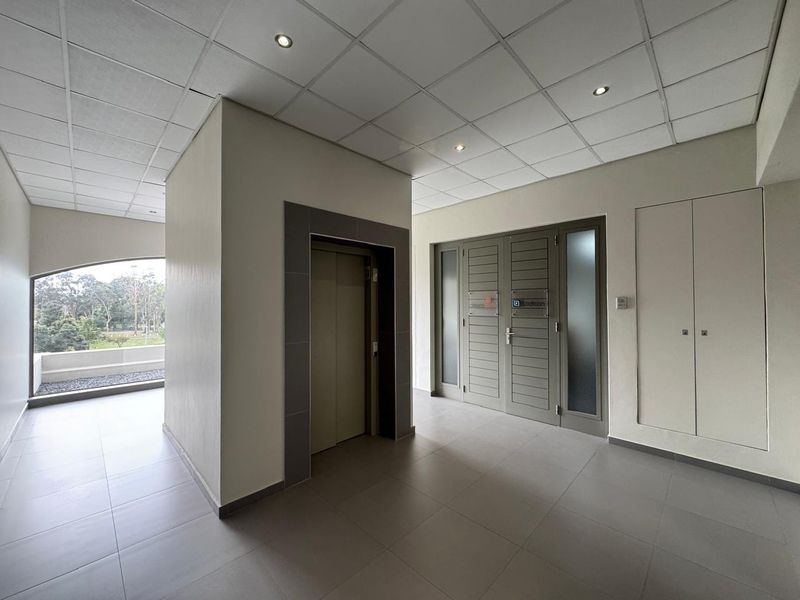 A clean and modern office building entrance lobby featuring tiled flooring, a central elevator, and integrated storage cupboards with recessed ceiling lighting.