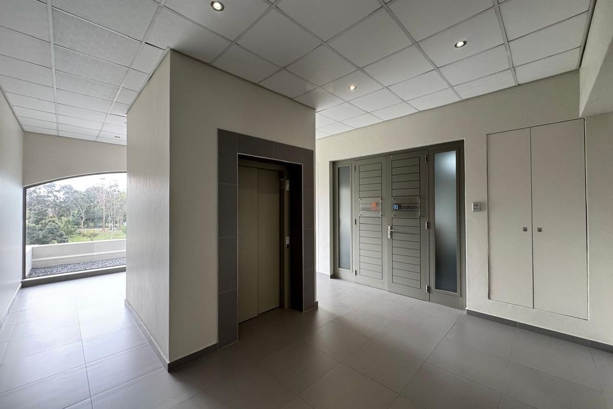 A clean and modern office building entrance lobby featuring tiled flooring, a central elevator, and integrated storage cupboards with recessed ceiling lighting.