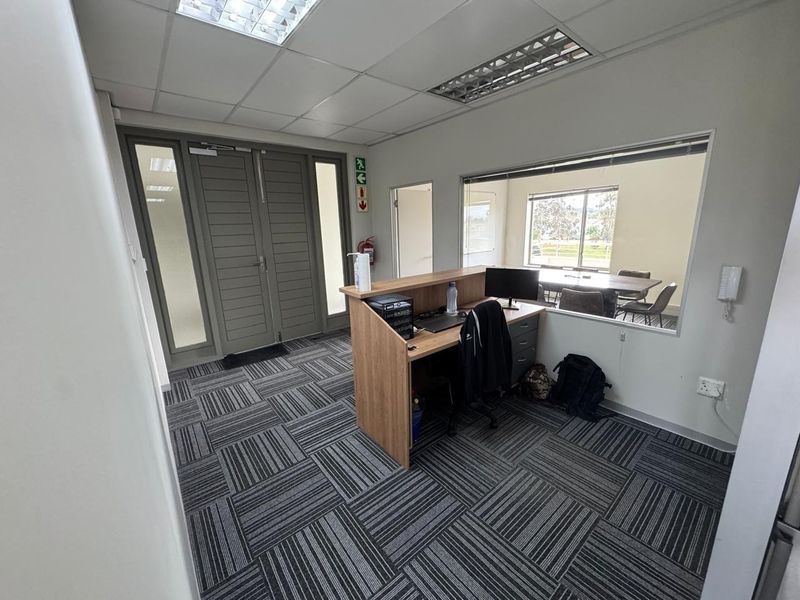Professional office reception area featuring a built-in desk, glass partition wall, modern carpet tiles, and double door access.