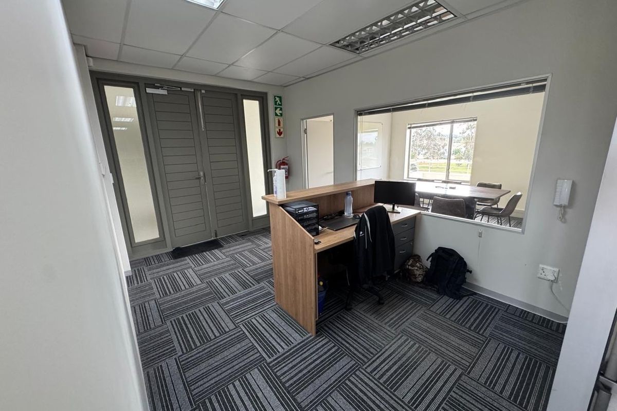 Professional office reception area featuring a built-in desk, glass partition wall, modern carpet tiles, and double door access.
