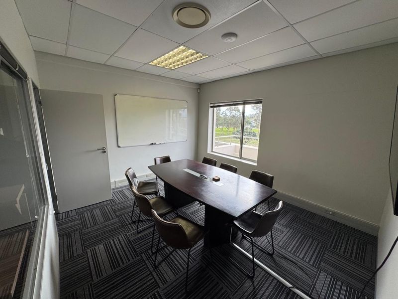 A functional office meeting room featuring carpet tiles, a suspended ceiling with recessed lighting, a wall-mounted whiteboard, and a glass partition wall.