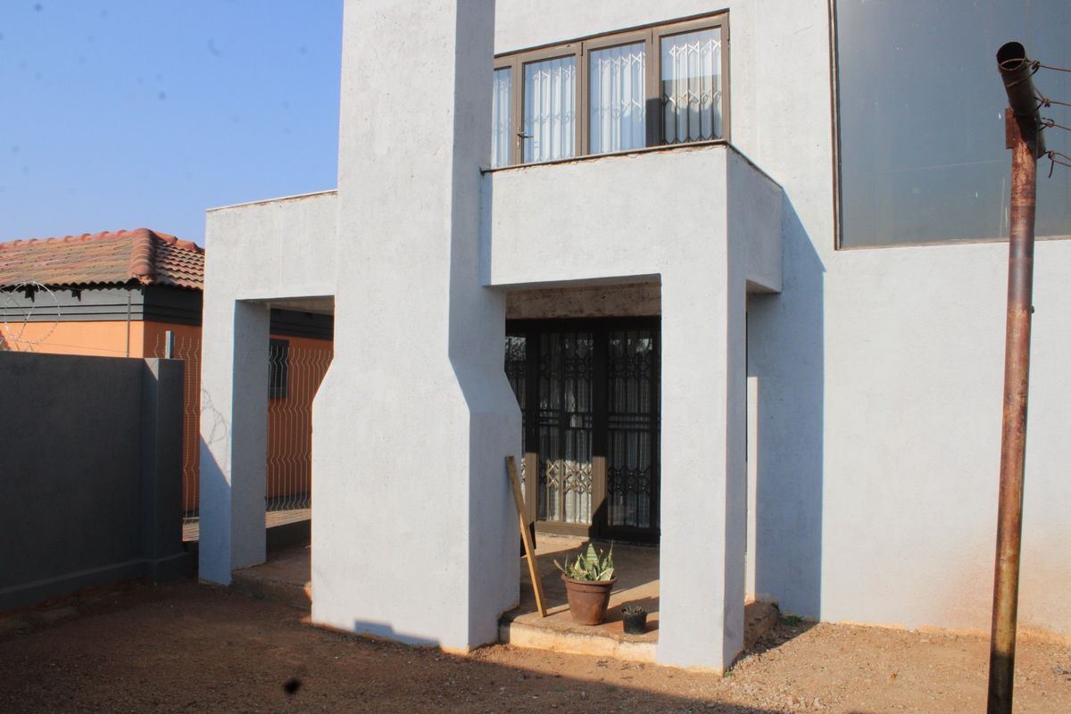 Rear view of the property featuring a covered patio area, external chimney breast, and security gates on the ground floor entrance.