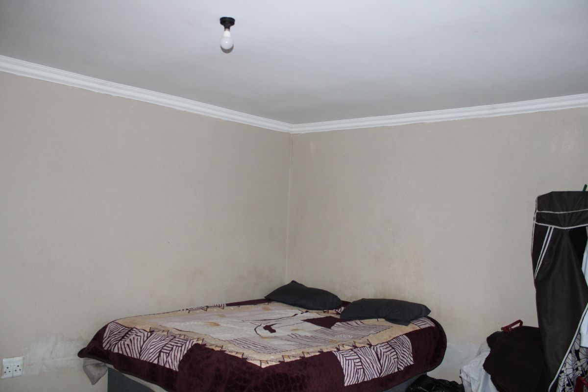 A bedroom featuring plain walls with visible damp staining and peeling paint, requiring maintenance and cosmetic updates.