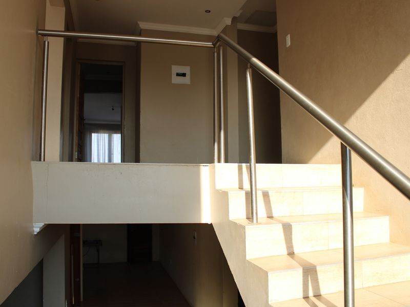 A bright hallway featuring a tiled staircase with a modern stainless steel balustrade, leading to an upper level landing area.