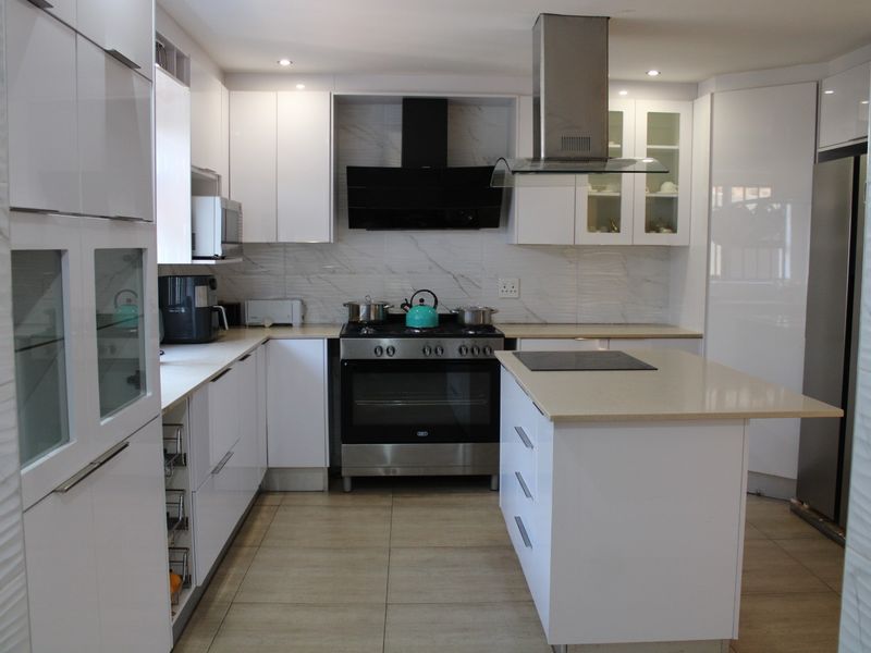 Modern kitchen featuring white gloss cabinetry, stone countertops, a central island, and high-quality stainless steel appliances with a marble-look splashback.