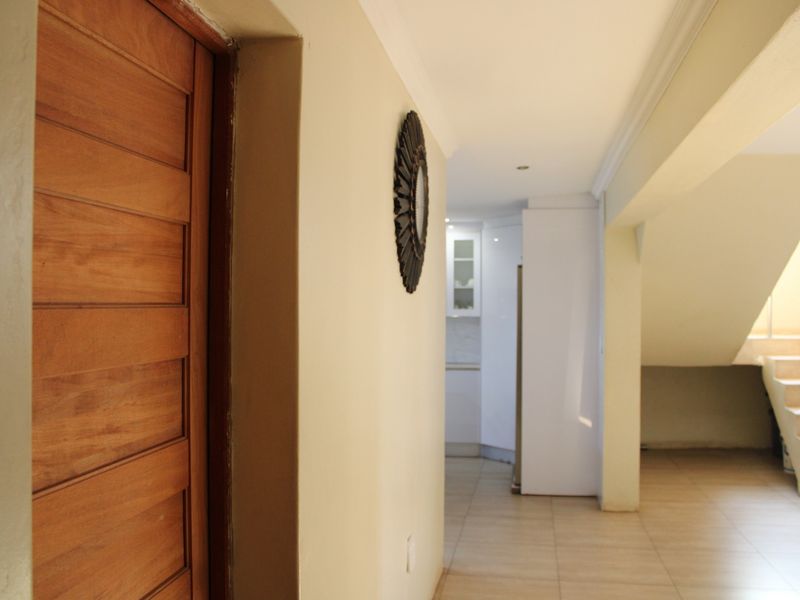 A bright hallway featuring tiled flooring, a wooden door, and a staircase leading to the upper level, with a view toward the kitchen area.