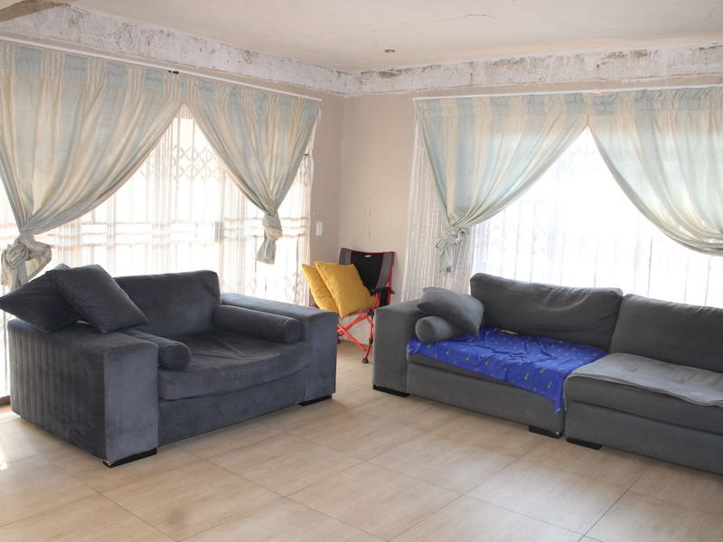Spacious living area featuring tiled flooring and large sliding glass doors with security gates, requiring cosmetic updates to the ceiling and wall finishes.