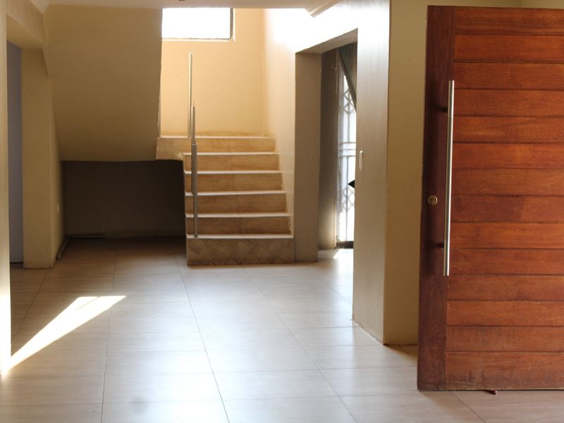 Spacious entrance hall featuring tiled flooring, a large wooden pivot door, and a staircase with a metal handrail.