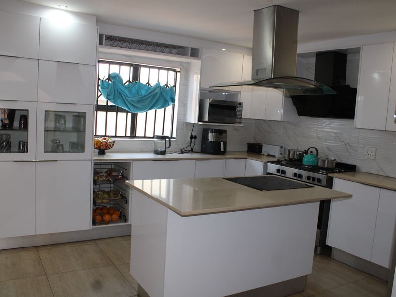 Modern kitchen featuring white gloss cabinetry, stone countertops, a central island with a hob, and integrated stainless steel appliances.