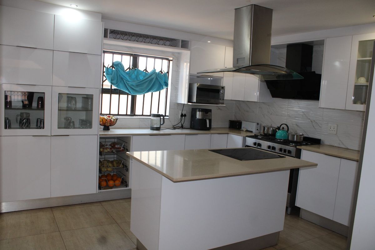 Modern kitchen featuring white gloss cabinetry, stone countertops, a central island with a hob, and integrated stainless steel appliances.