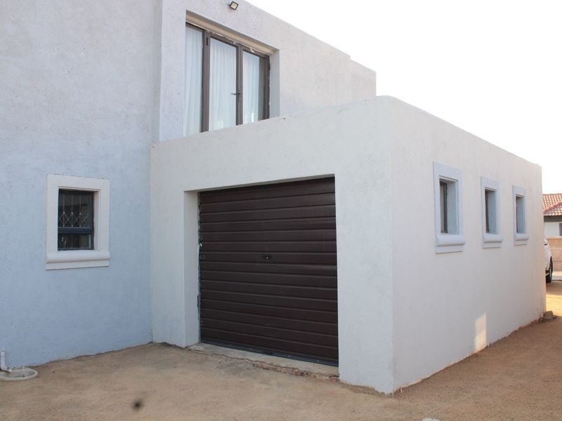 Exterior view of a residential garage featuring a brown roller door and plastered walls with multiple windows.
