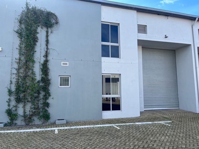 Industrial unit exterior featuring a large roller shutter door, paved parking area, and two-story aluminium framed windows.