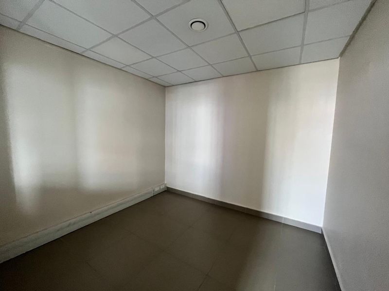 A clean, empty office space featuring a suspended ceiling, recessed lighting, and neutral tiled flooring, suitable for a professional workspace.