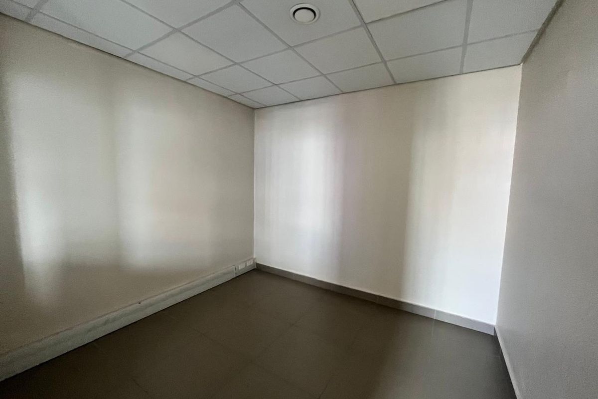 A clean, empty office space featuring a suspended ceiling, recessed lighting, and neutral tiled flooring, suitable for a professional workspace.