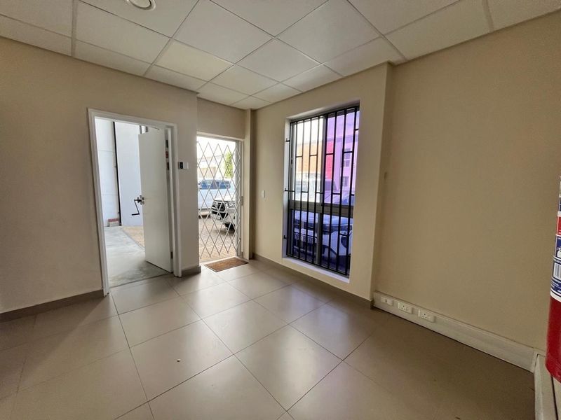 A clean, empty office space featuring tiled flooring, a suspended ceiling, and secure window and door access.