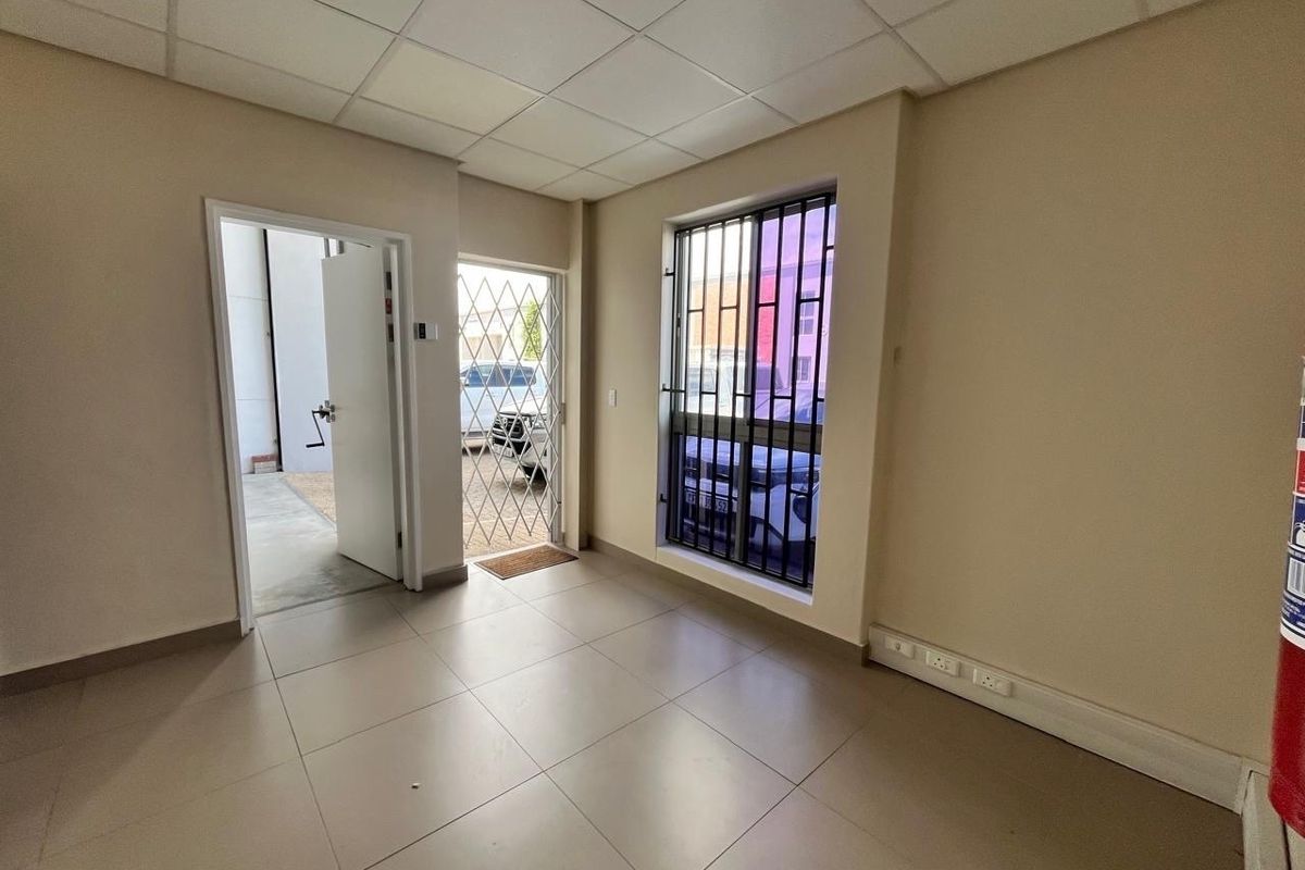 A clean, empty office space featuring tiled flooring, a suspended ceiling, and secure window and door access.
