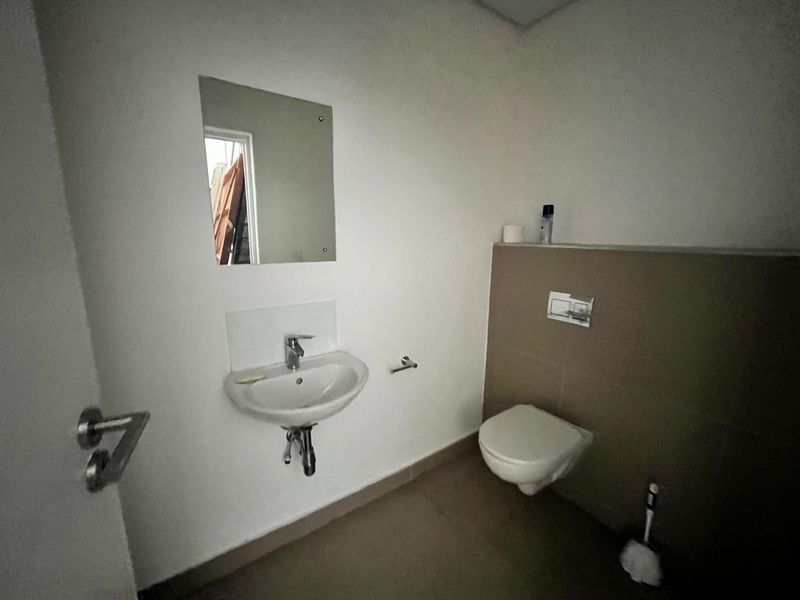 A clean, minimalist guest bathroom featuring a wall-mounted toilet, wall-mounted basin with chrome fixtures, and neutral tiled finishes.
