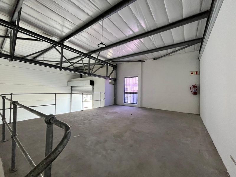 An open-plan mezzanine level in an industrial unit featuring exposed steel trusses, concrete flooring, and a secure roller shutter access point.