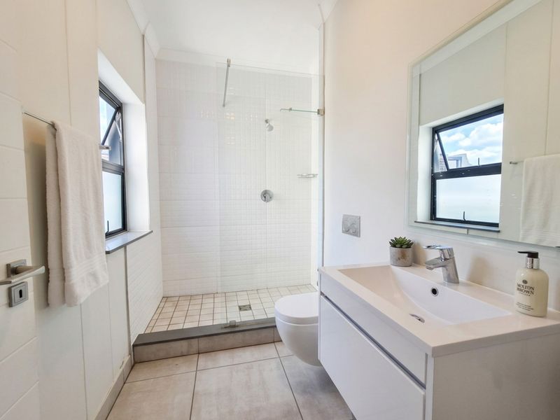 Modern bathroom featuring a walk-in shower with glass screen, wall-mounted toilet, and a sleek vanity unit with basin.