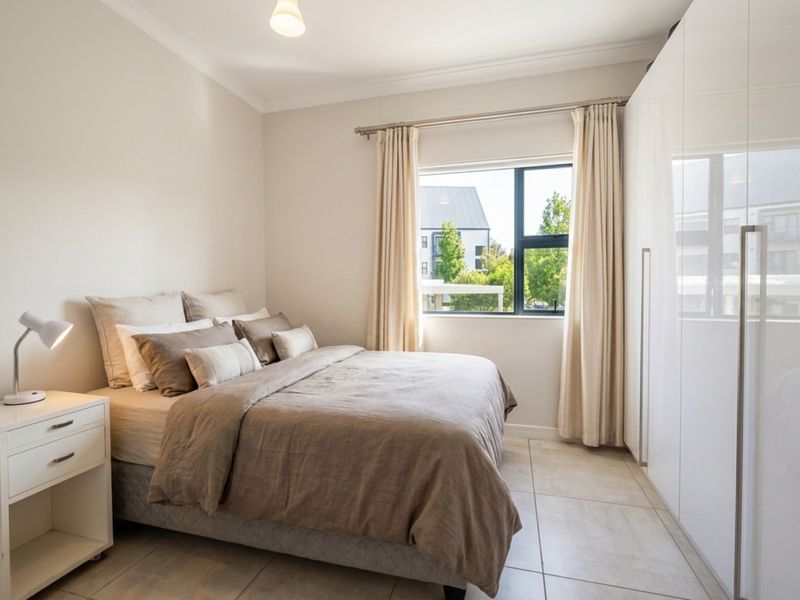 A well-maintained bedroom featuring neutral tiled flooring, a large built-in wardrobe, and natural light through an aluminium-framed window.