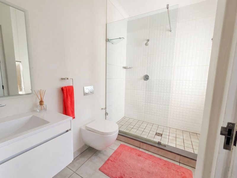 Modern bathroom featuring a wall-mounted toilet, a sleek vanity with integrated sink, and a spacious walk-in shower with a glass screen.