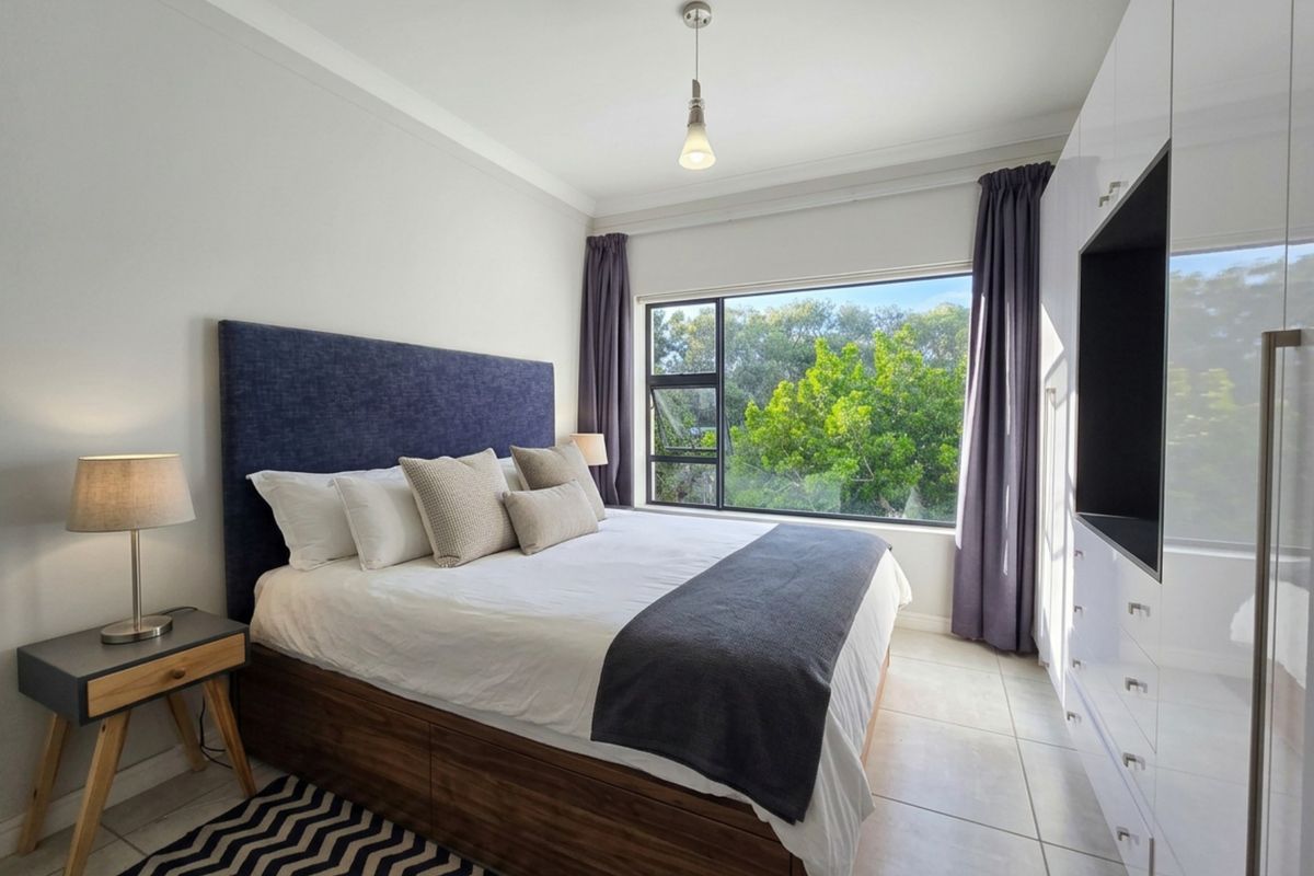 A well-maintained bedroom featuring large windows with garden views, tiled flooring, and extensive built-in cabinetry for storage.