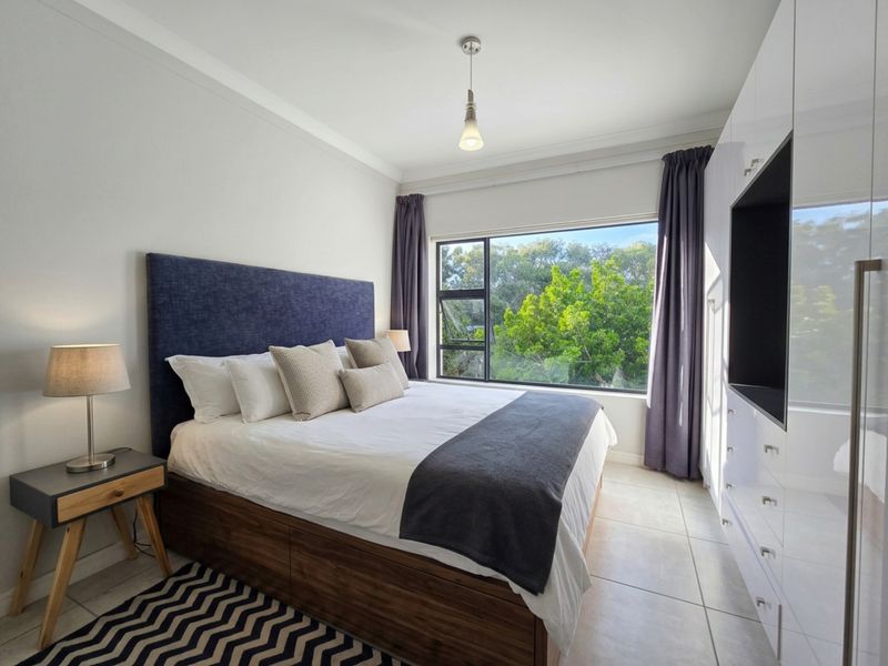 A well-maintained bedroom featuring large windows with garden views, tiled flooring, and extensive built-in cabinetry for storage.