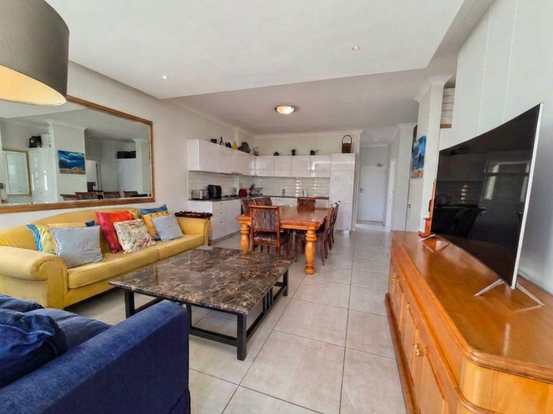 Open-plan living and dining area featuring tiled floors, recessed lighting, and a functional kitchen with white cabinetry and a subway tile backsplash.