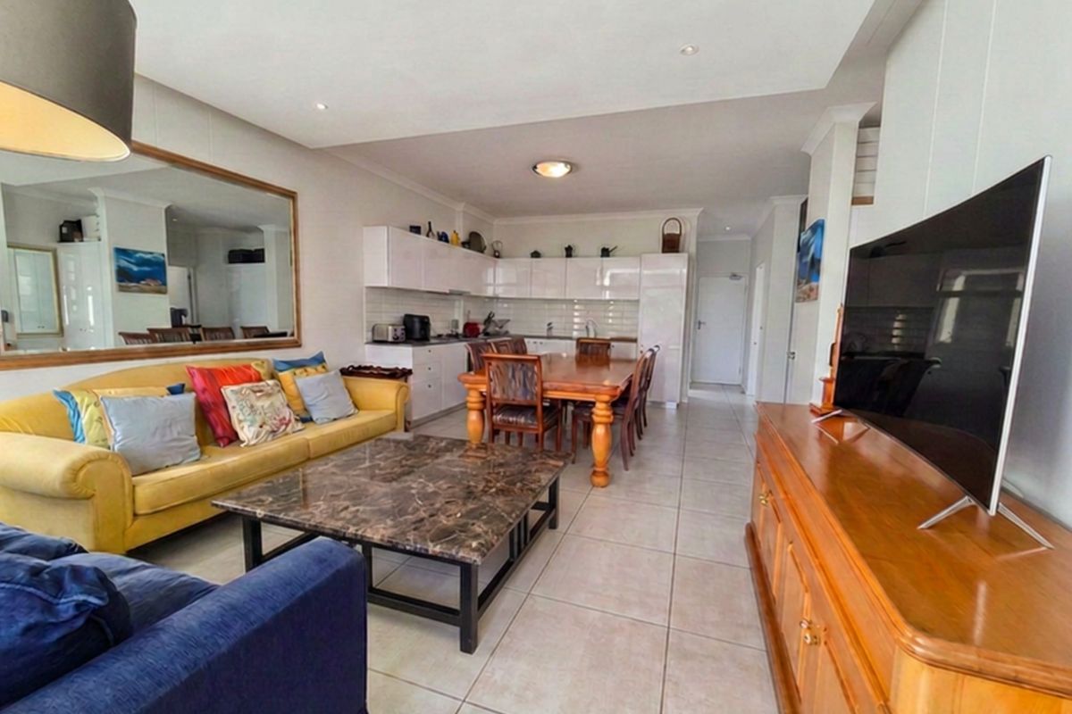 Open-plan living and dining area featuring tiled floors, recessed lighting, and a functional kitchen with white cabinetry and a subway tile backsplash.