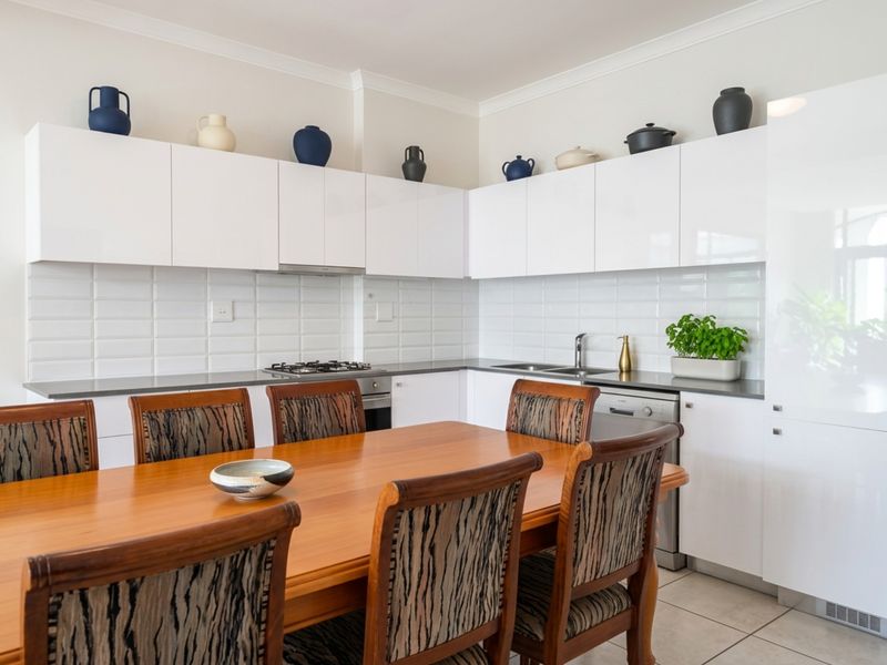 Modern open-plan kitchen featuring white gloss cabinetry, subway tile backsplash, integrated appliances, and a gas hob, seamlessly flowing into the dining area.