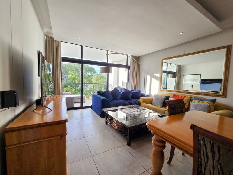 A bright and spacious living room featuring large sliding glass doors that open onto a balcony, tiled flooring, and a modern recessed ceiling design.