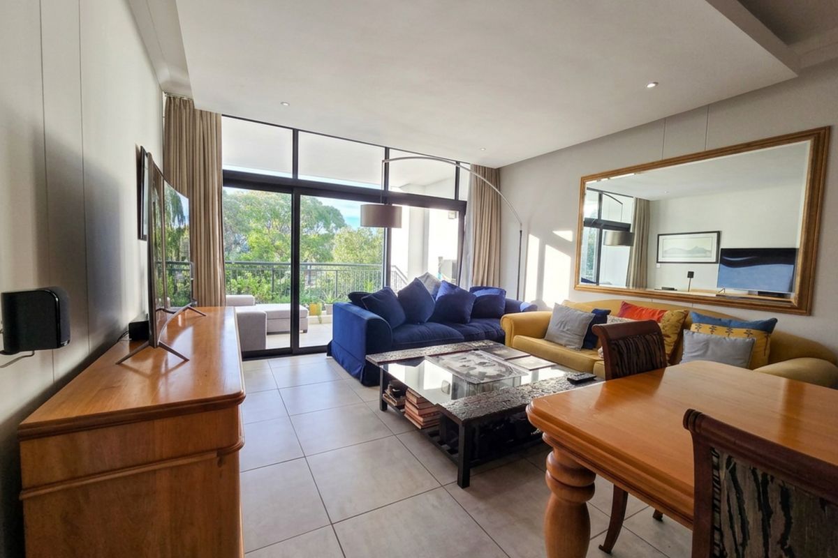 A bright and spacious living room featuring large sliding glass doors that open onto a balcony, tiled flooring, and a modern recessed ceiling design.