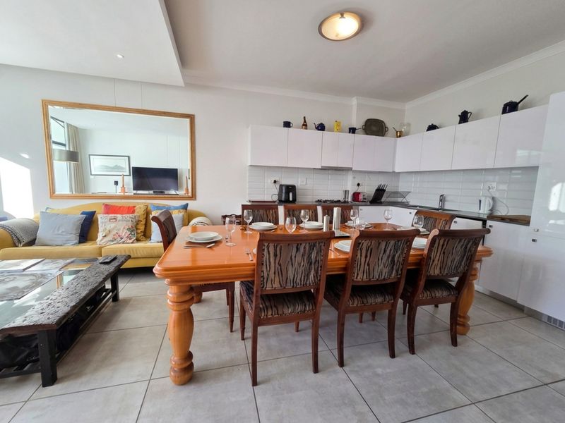 Open-plan living and dining area featuring a modern kitchen with white gloss cabinetry, subway tile backsplash, and neutral ceramic floor tiles throughout.