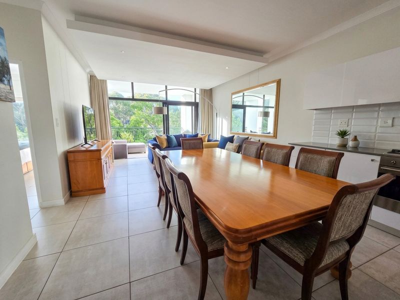 Spacious open-plan living and dining area featuring tiled floors, a modern kitchen with built-in appliances, and large sliding doors leading to a balcony.