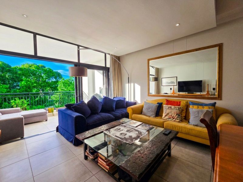 A bright, open-plan living room featuring large sliding glass doors that lead to a balcony, providing ample natural light and a view of greenery.