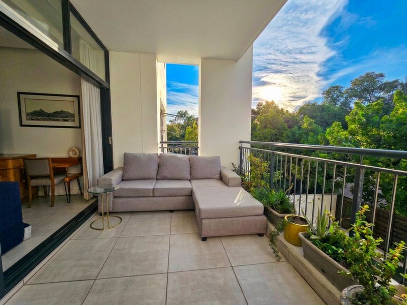 A covered balcony featuring tiled flooring and a metal balustrade, offering an outdoor living space accessible through large sliding glass doors.