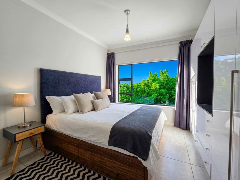 A well-maintained bedroom featuring built-in cupboards, tiled flooring, and a large window with pleasant green views.