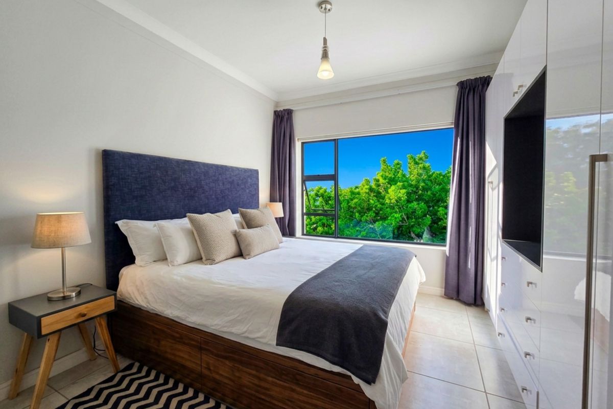 A well-maintained bedroom featuring built-in cupboards, tiled flooring, and a large window with pleasant green views.